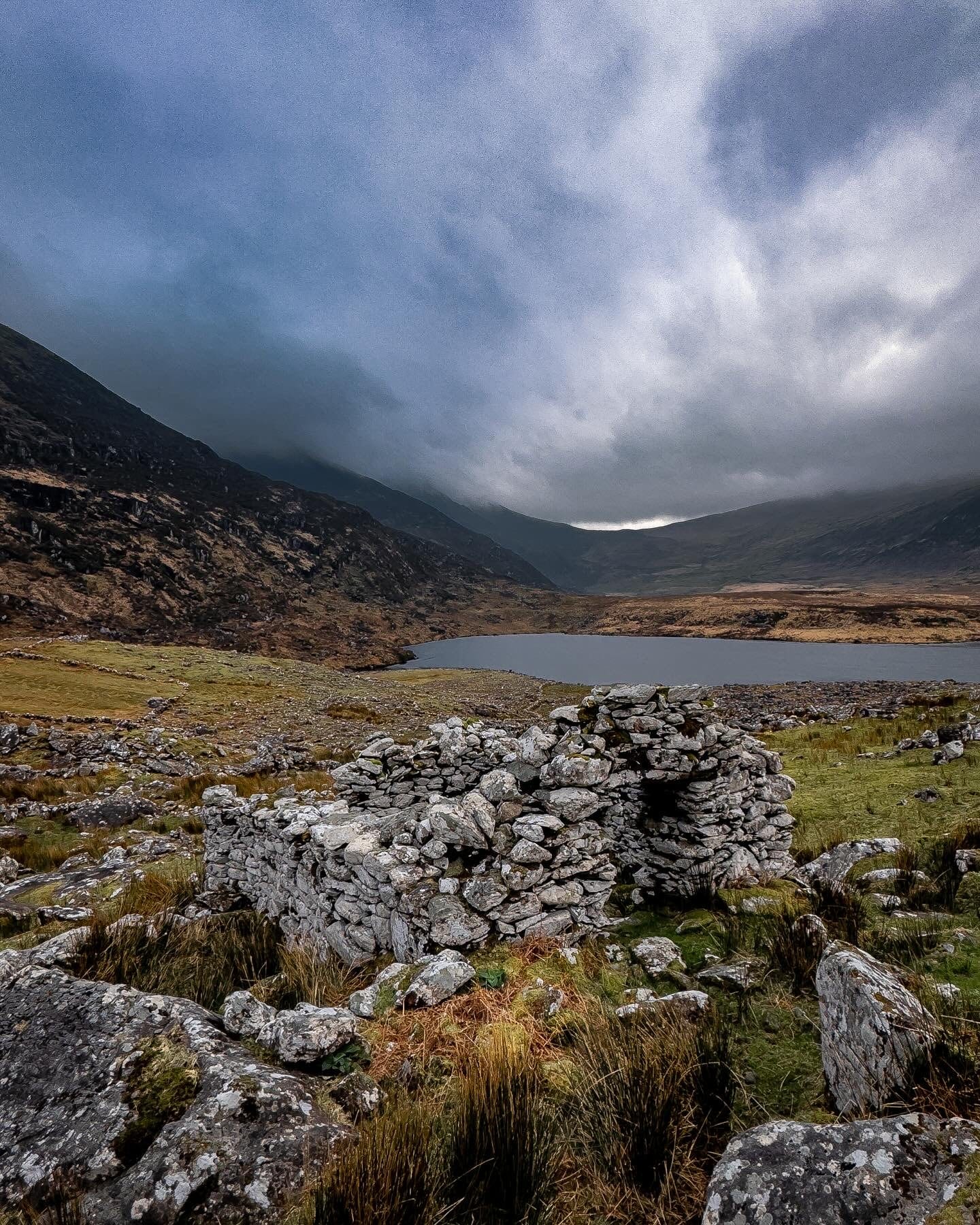 Old stone ruins beside a mountain lake under dark cloud