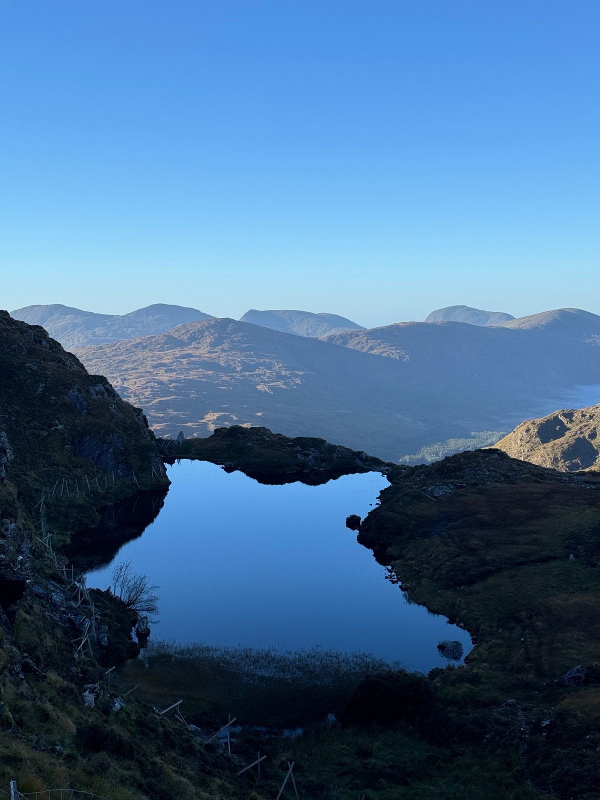 A small dark lake between rocky banks, with mountains on the horizon