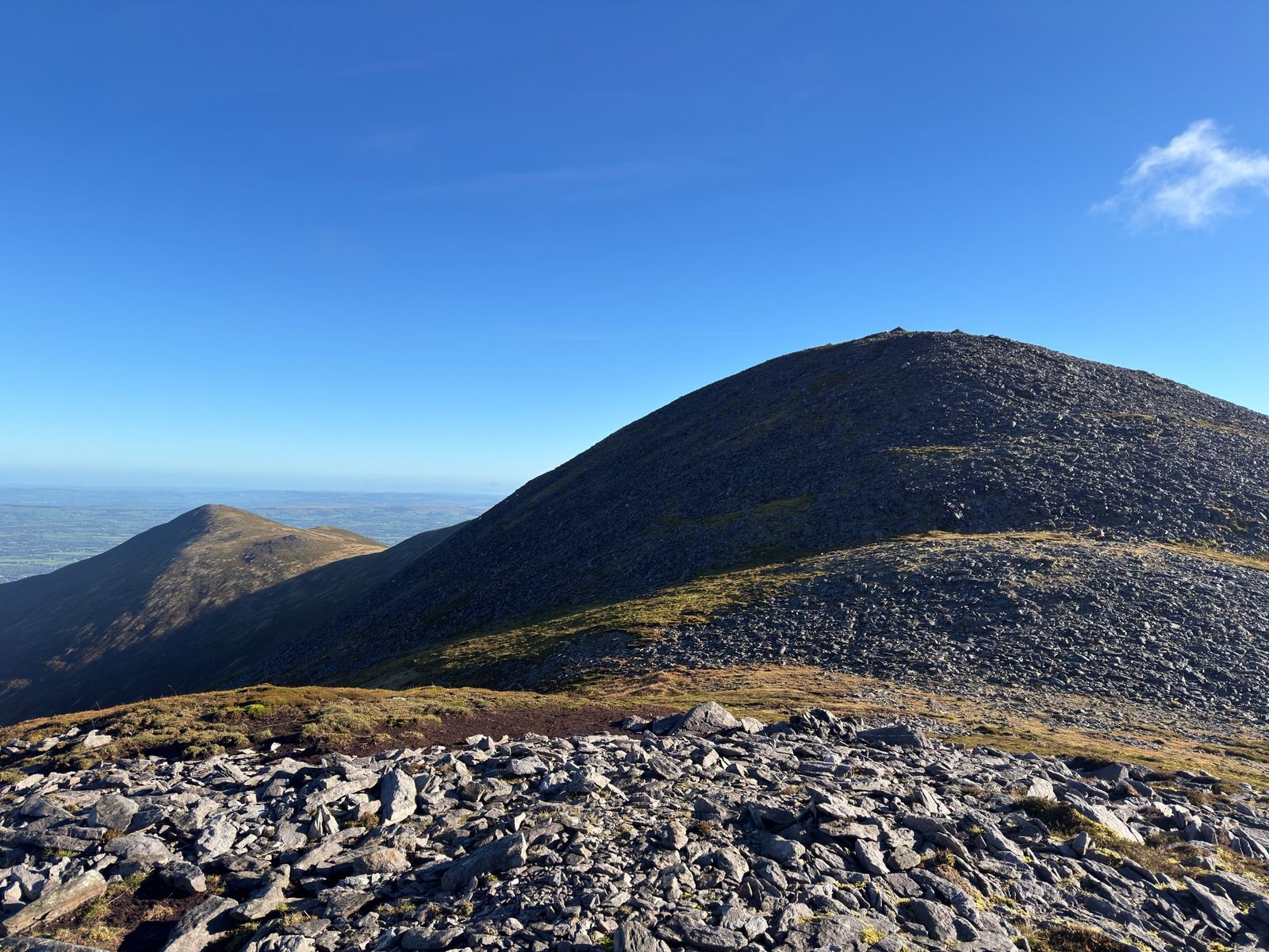 A rounded summit covered in grey slate, rising against a blue sky