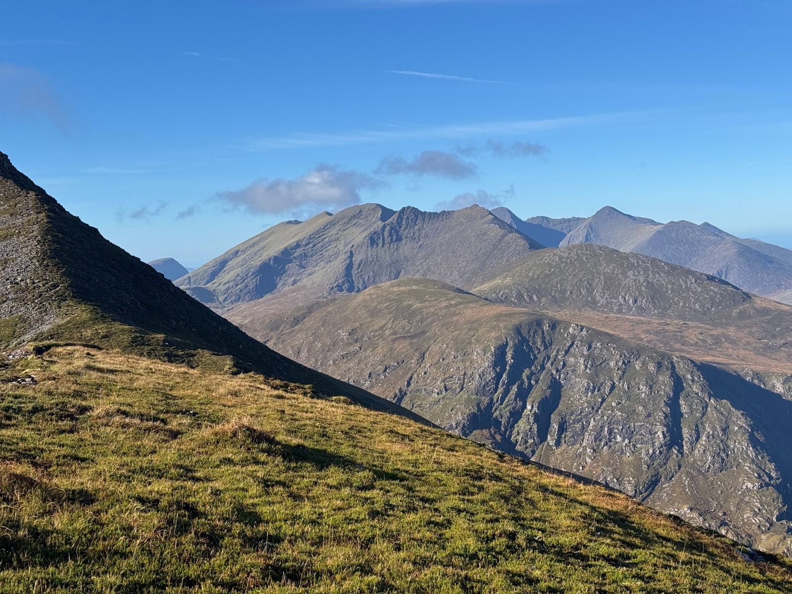A steep grassy slope in the foreground with the jagged ridges of the Reeks beyond