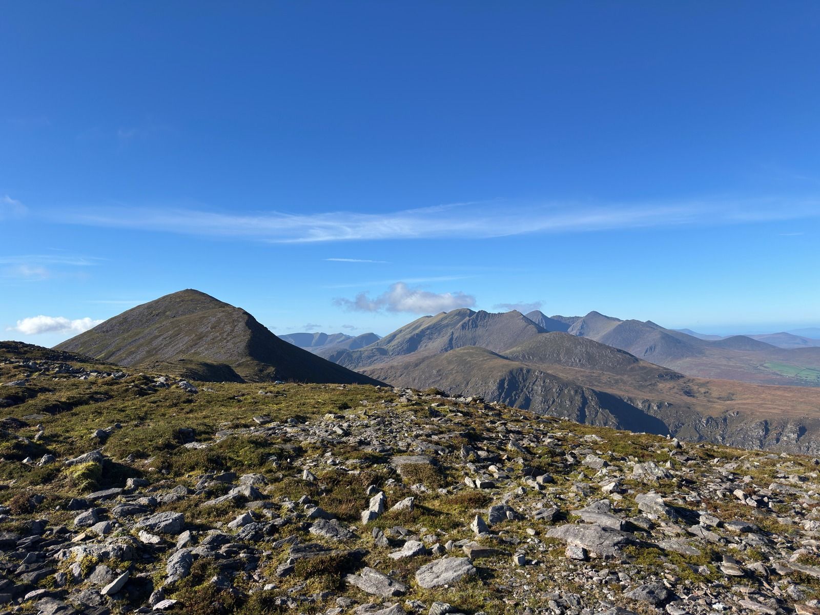 A pointed peak rising above slate-strewn ground, with more mountains beyond