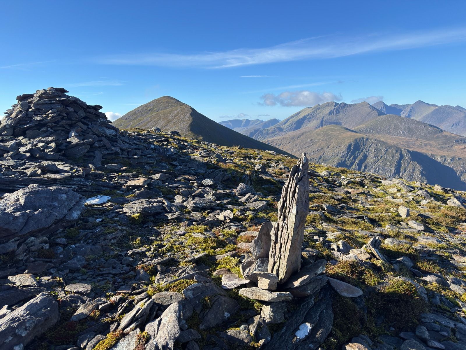 A cairn of stacked slate with a thin upright slab beside it, and peaks beyond