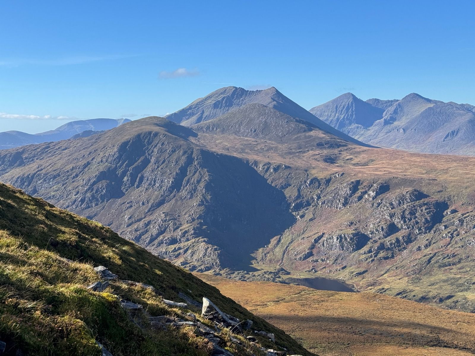 A mountain falling steeply to a small lake on a valley floor, with higher peaks behind
