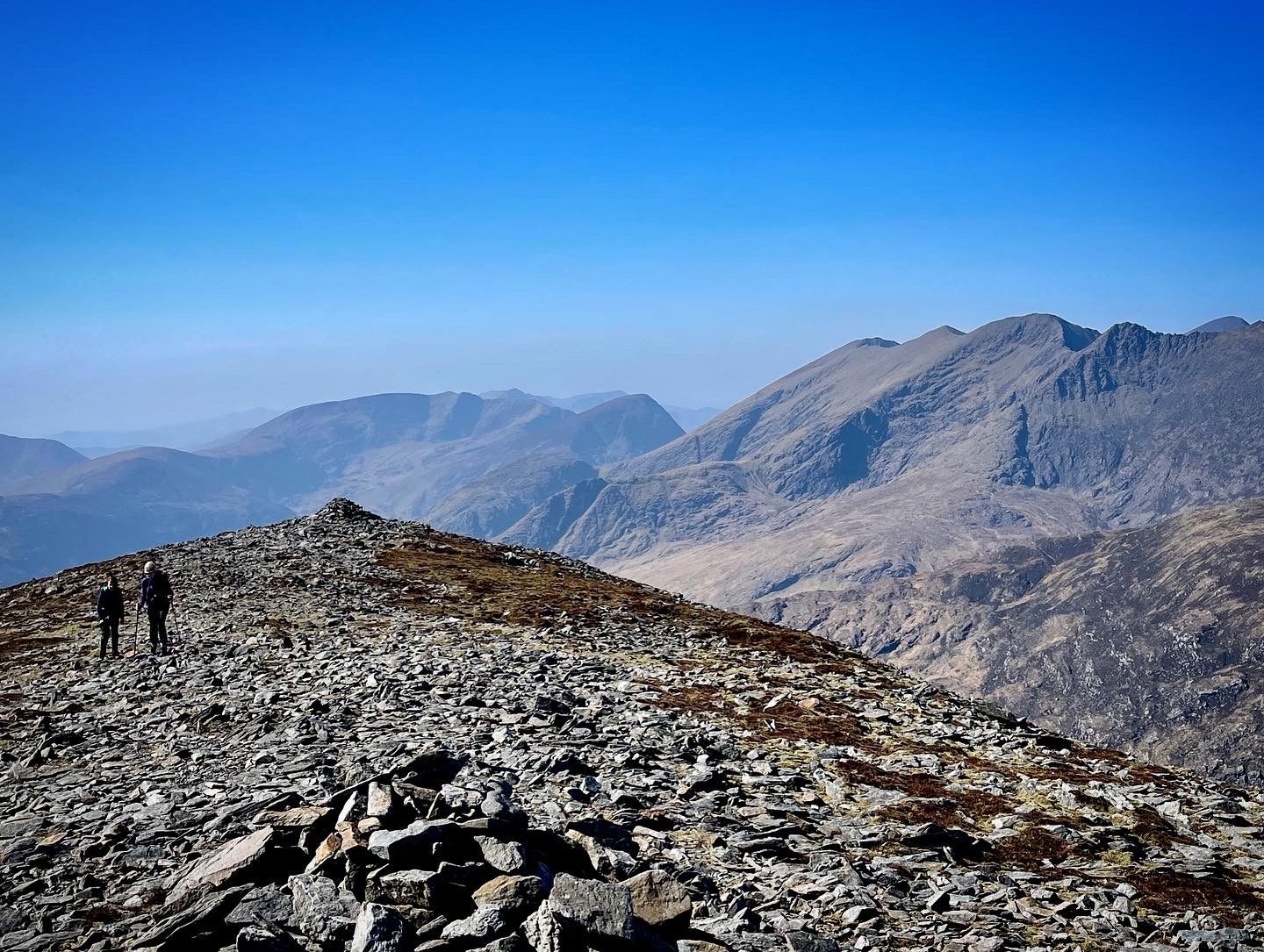 Two walkers on a broad slate ridge, with the Reeks beyond