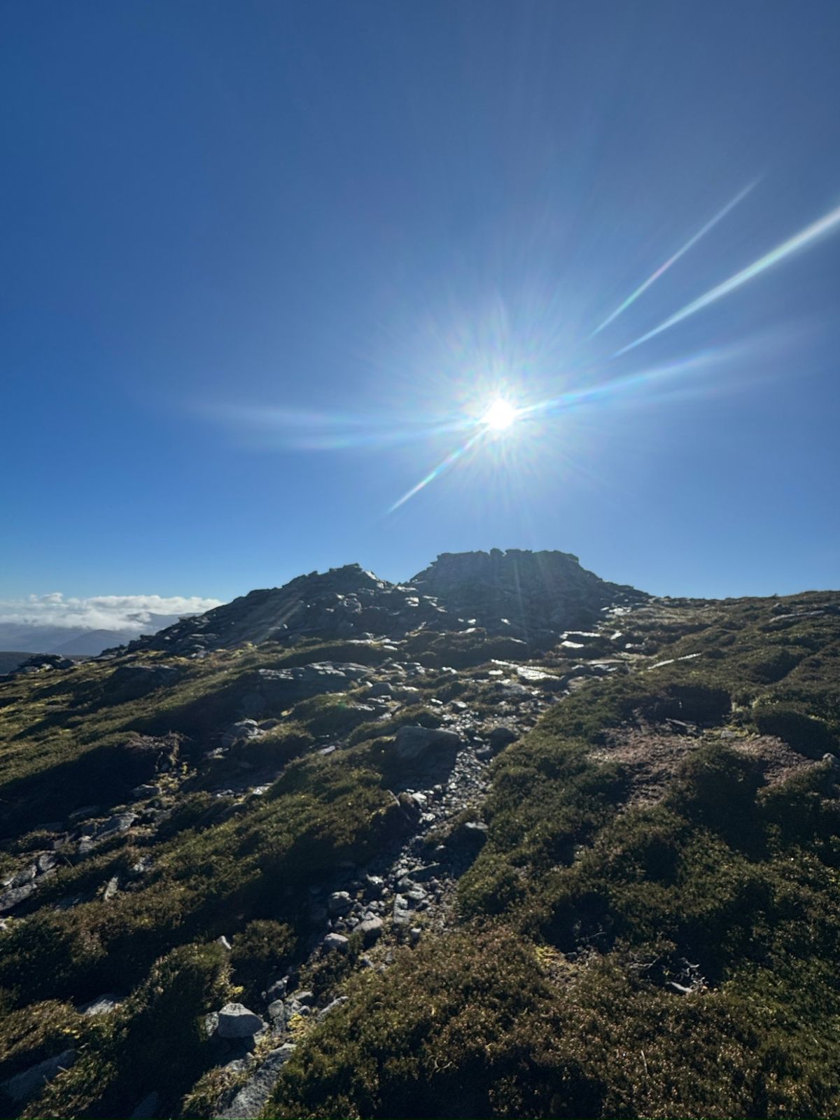 The sun low over a rocky summit, with a stony path through heather leading up to it