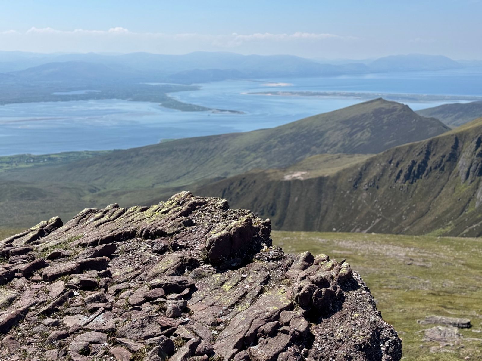Red rock and the high ridge of Barr Trí gCom above the distant Kerry coast