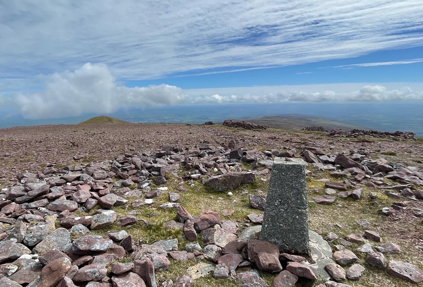Warm light on the summit trig pillar with distant mountain ridges beyond