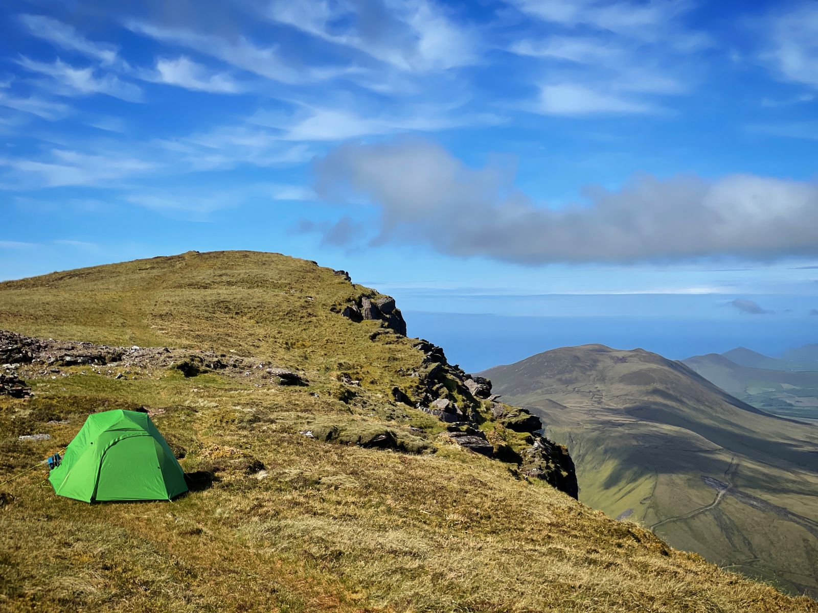 A small green tent pitched beside a steep high ridge