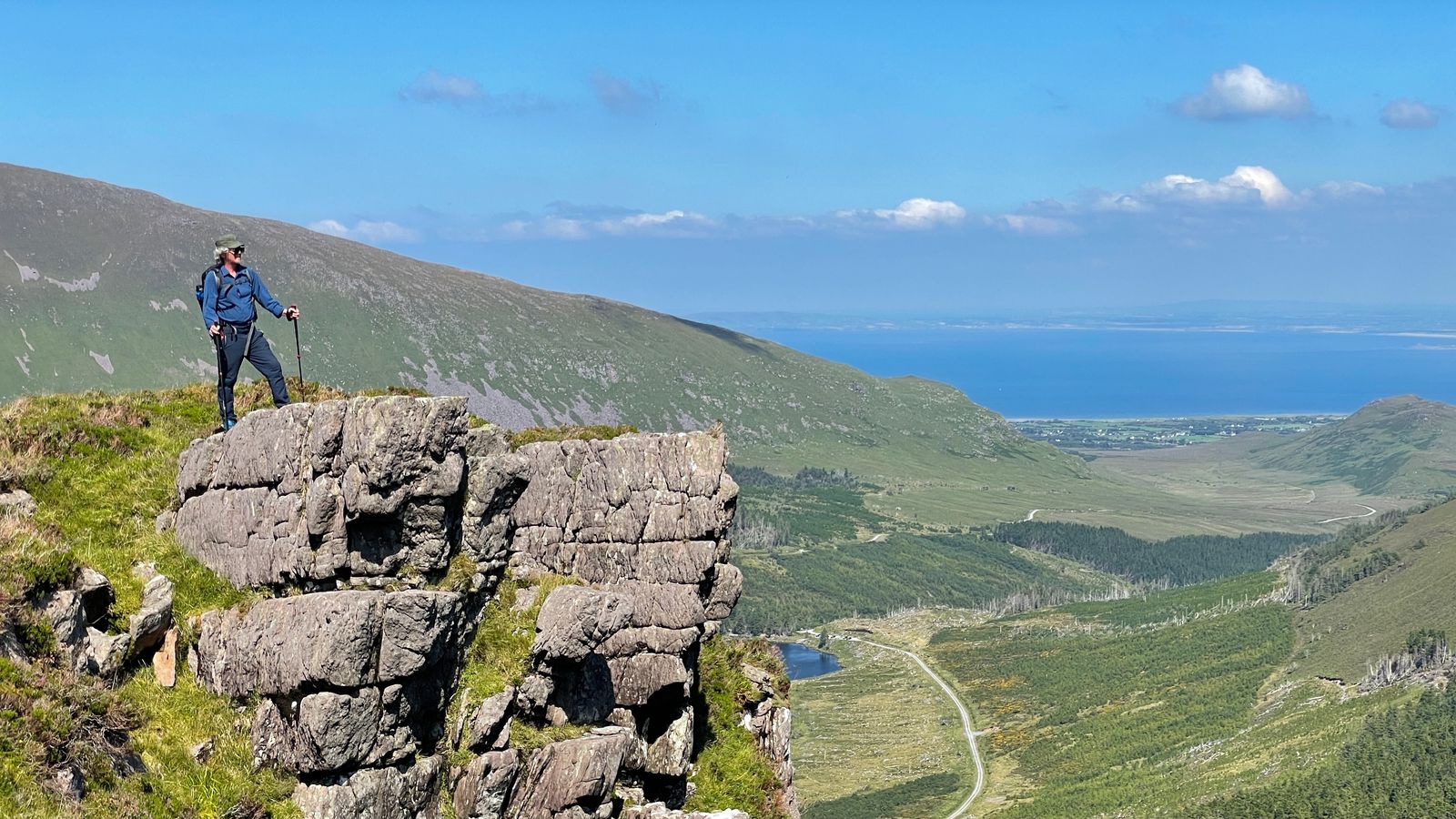 A hillwalker standing on a rocky outcrop above Glanteenassig with Brandon Bay beyond