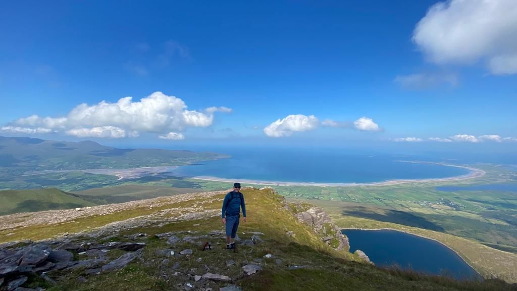 A hillwalker crossing the ridge above a corrie lough and Brandon Bay