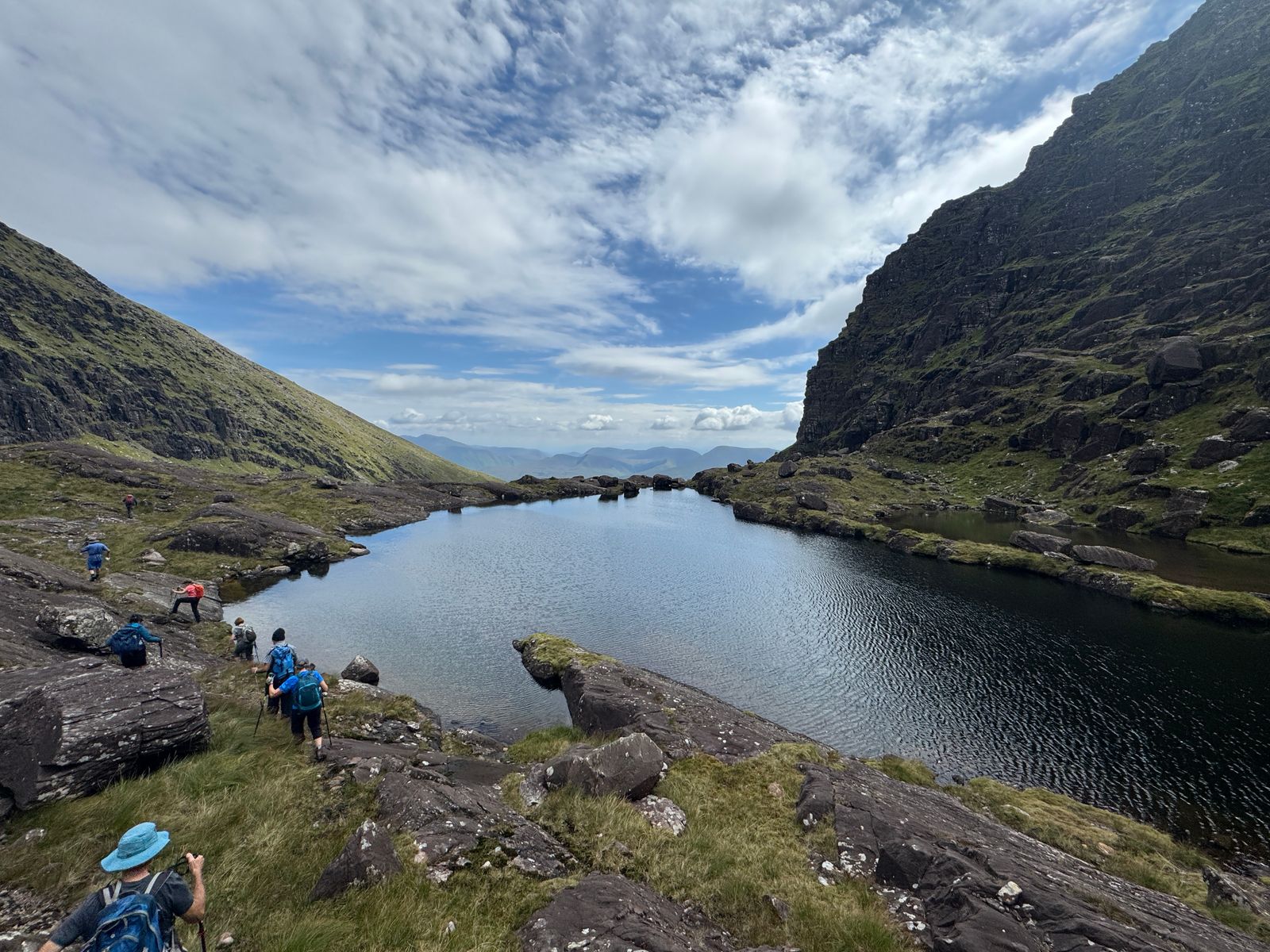 Walkers beside an upper corrie lake beneath a dark rock wall