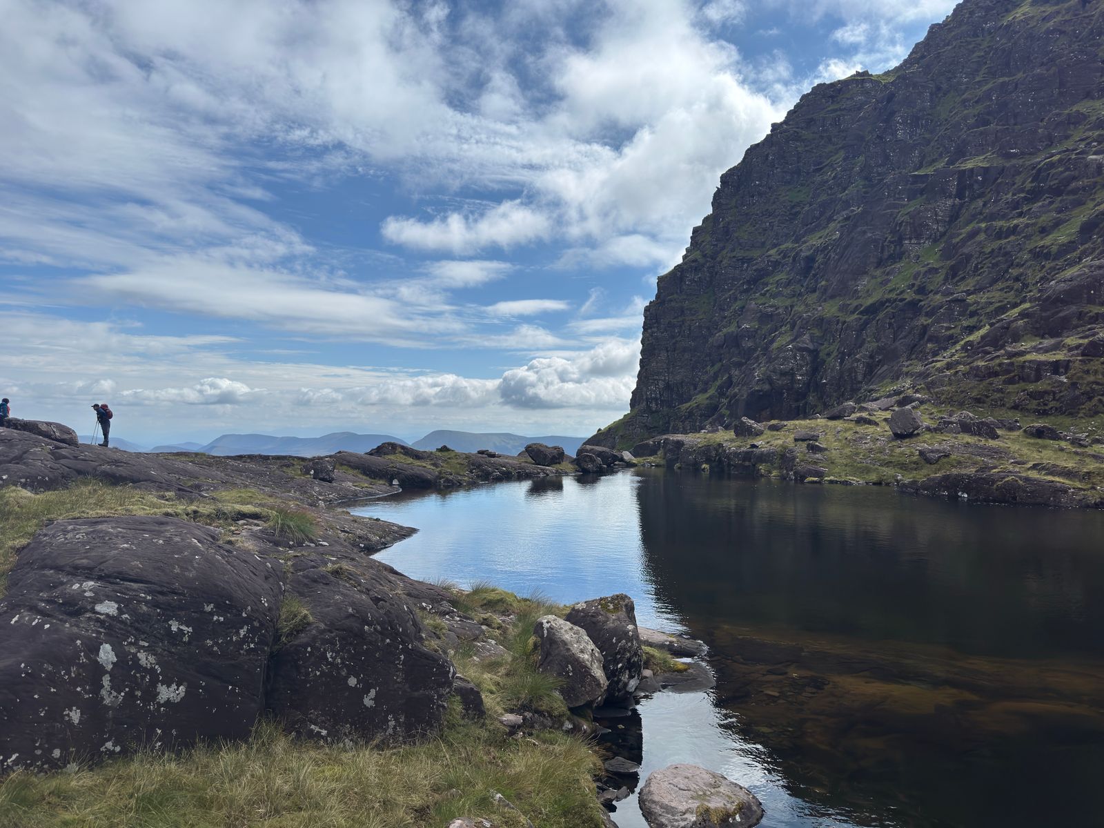Walkers crossing rock beside a reflective mountain lake