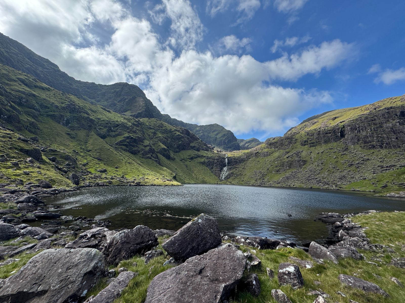 A corrie lake held beneath steep green mountain walls