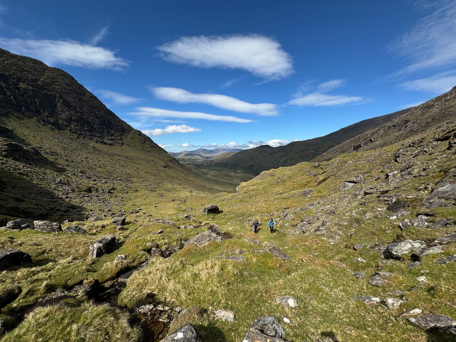 Walkers crossing the rough green valley beneath steep mountain slopes