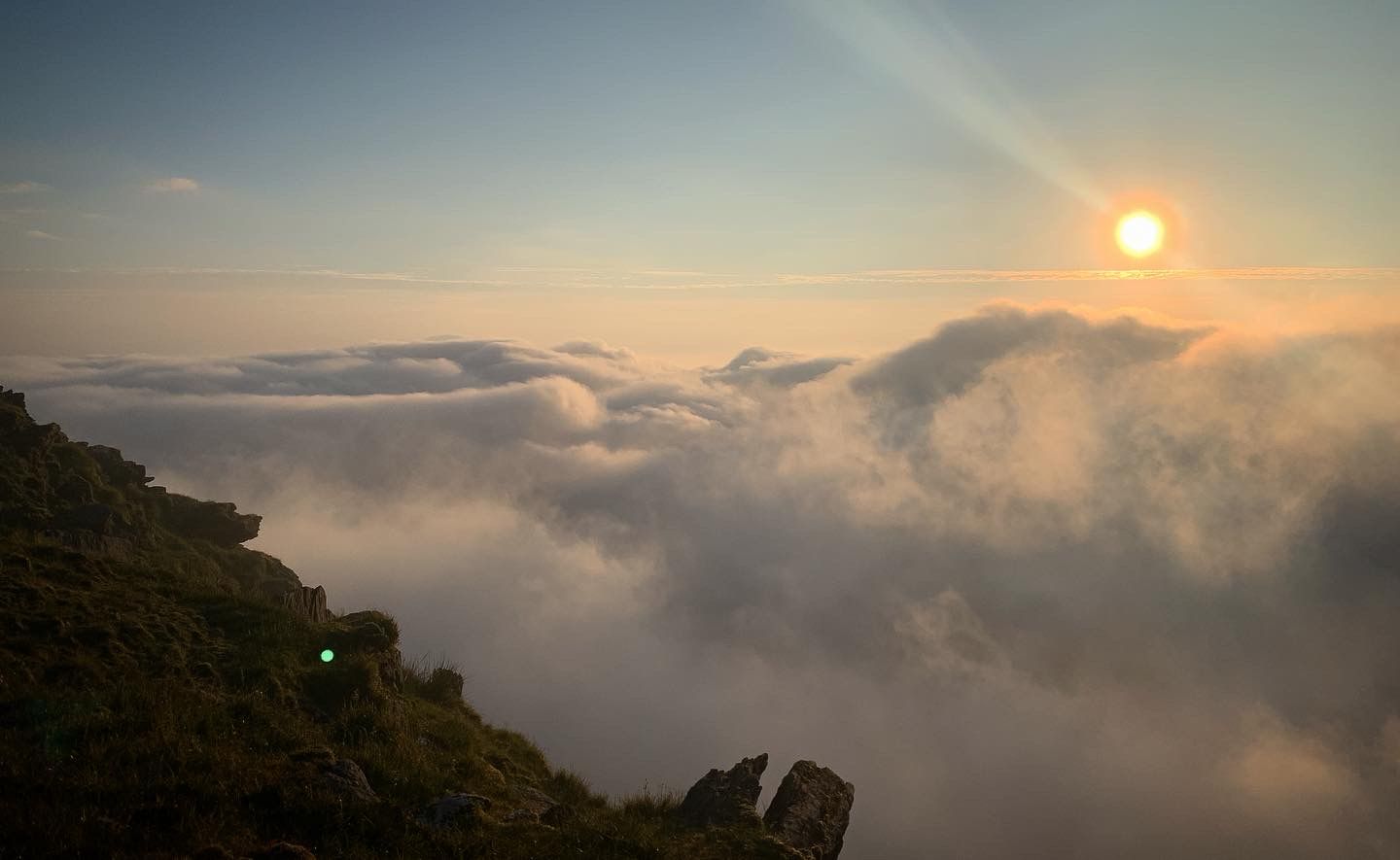 The sun breaking above a bank of cloud beside the steep mountain slope