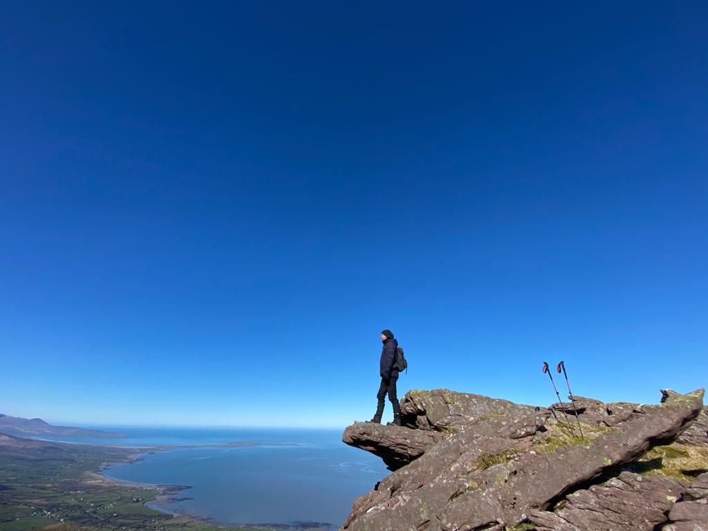 A walker silhouetted on Fionn Mac Cumhaill’s Chair above the bay