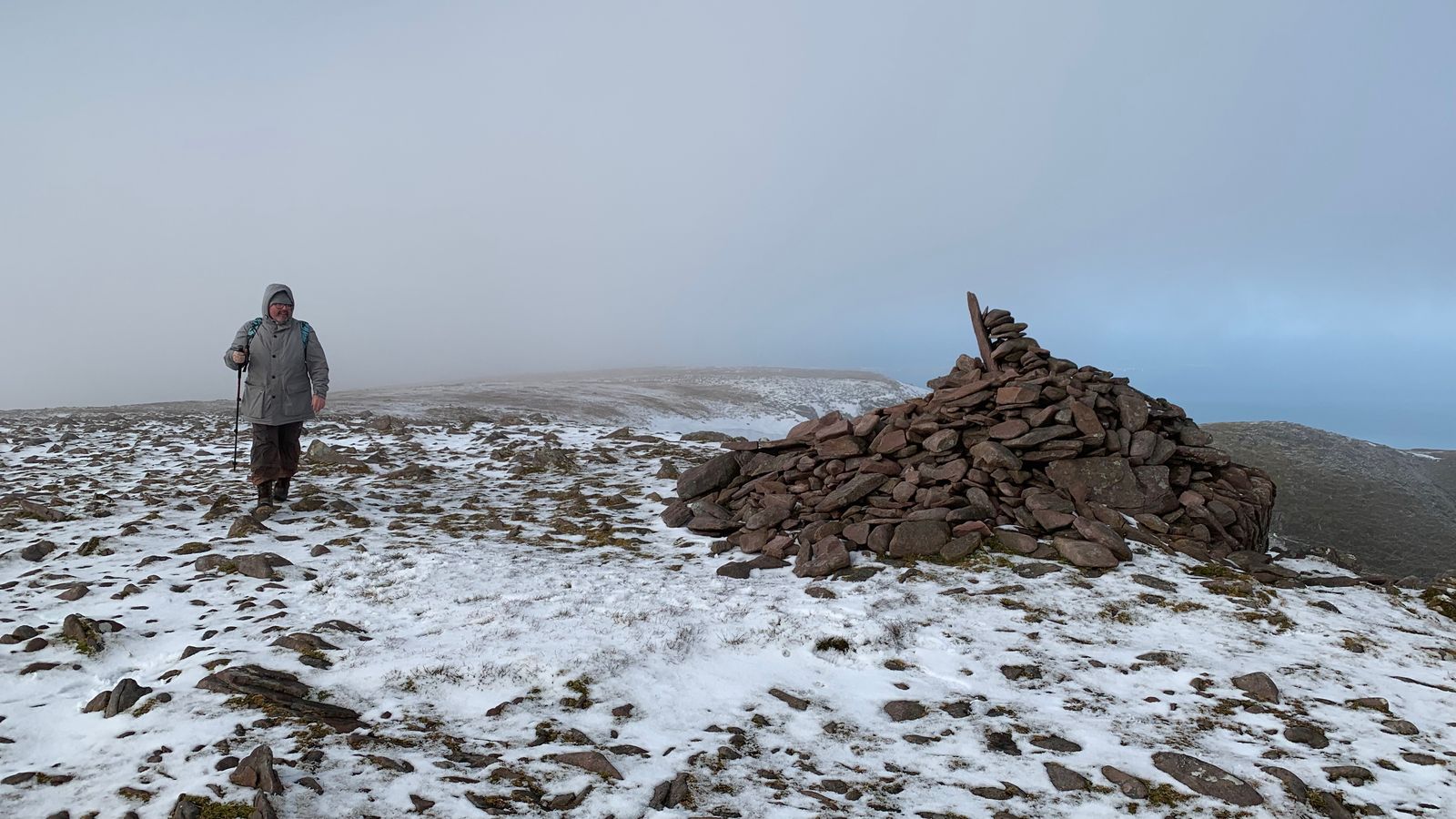 A walker beside the summit cairn on snow-covered high ground