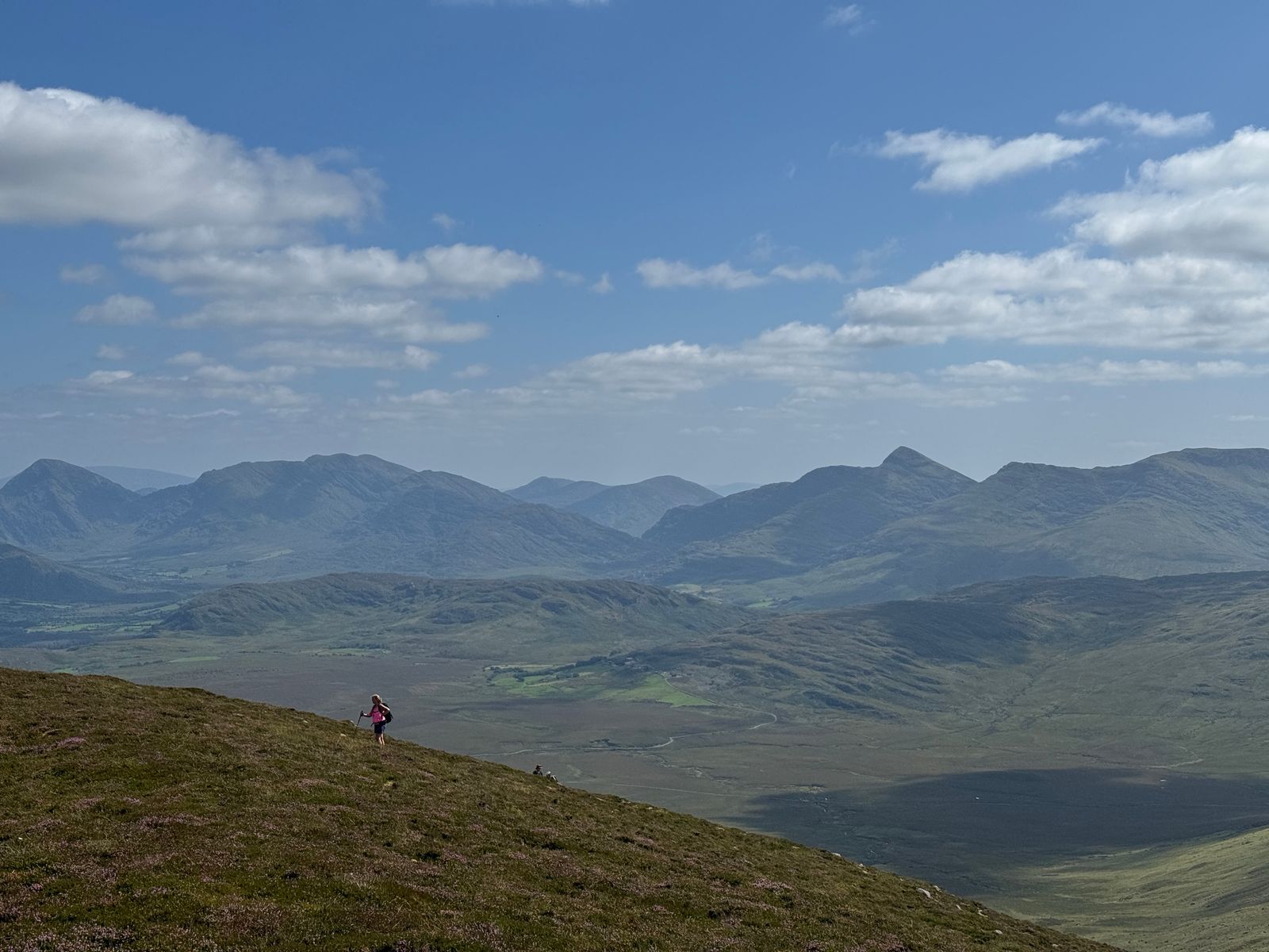A lone walker on the open slope above a broad mountain valley
