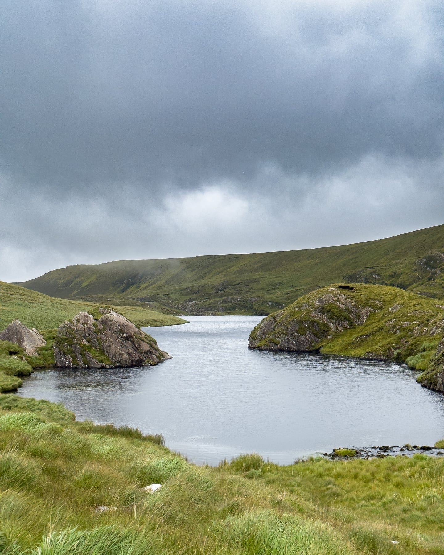 A mountain lake and rocky islands beneath a dark incoming sky