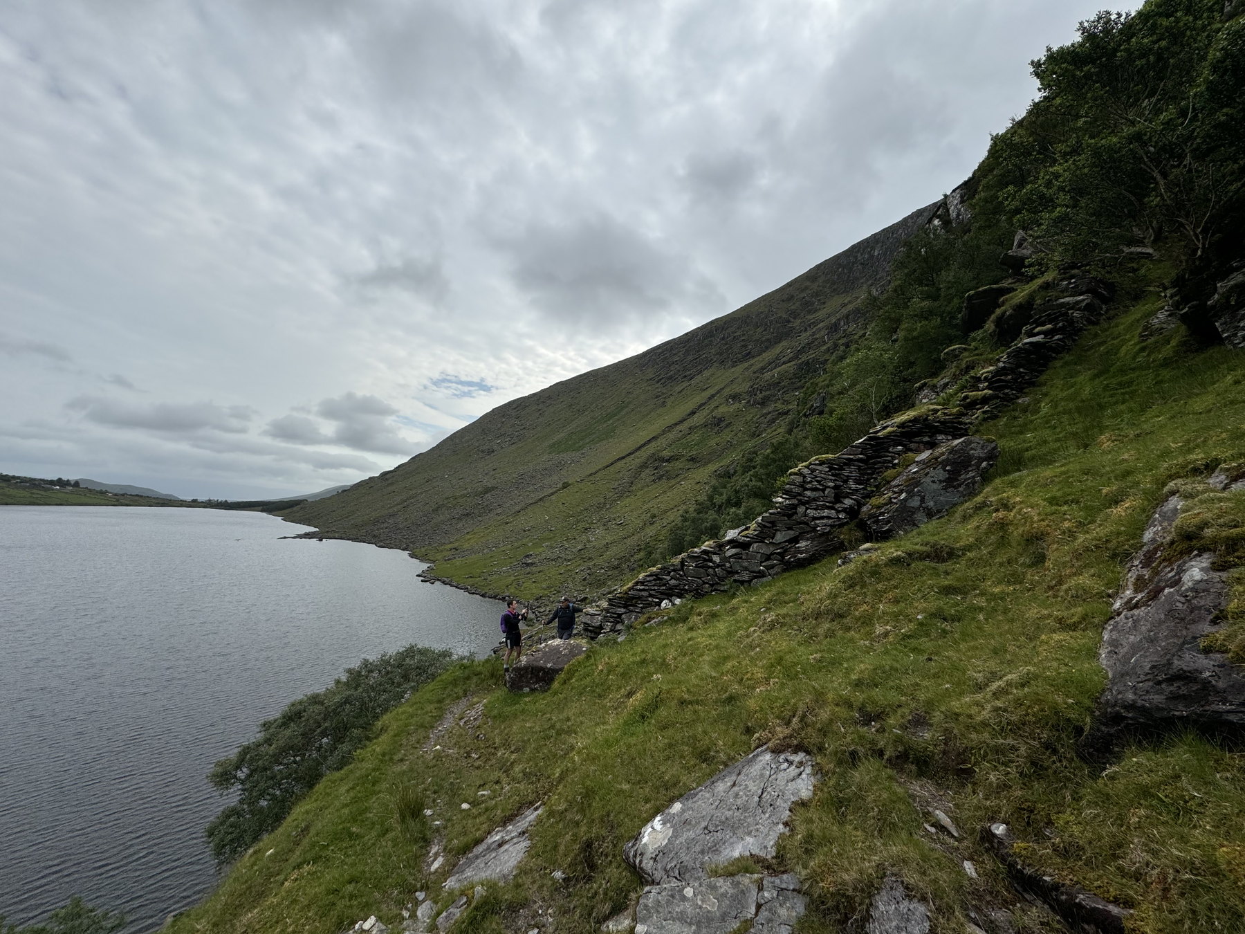 Walkers traversing steep green ground beside a mountain lake