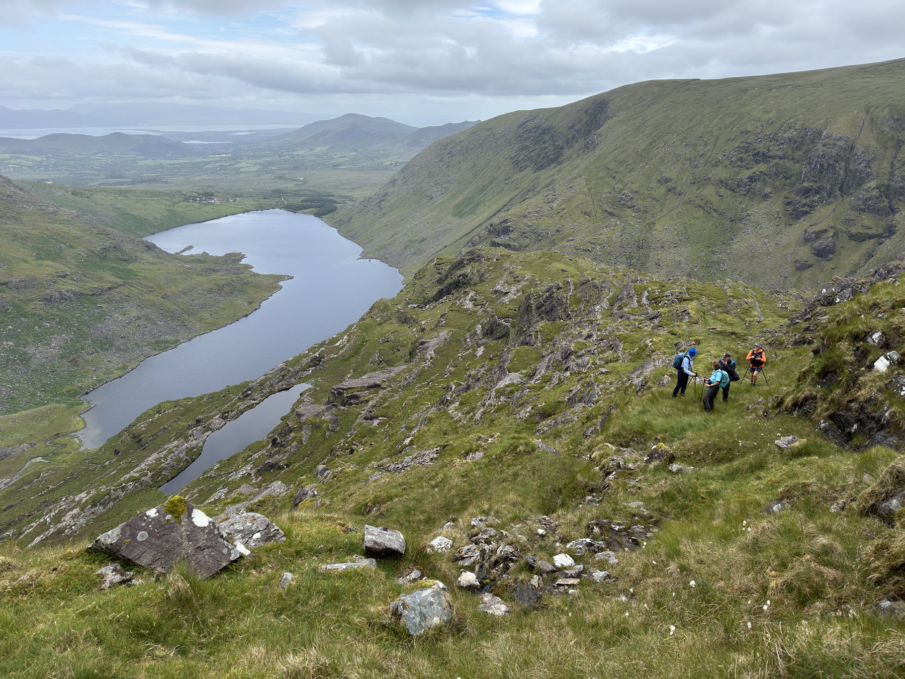 A long mountain lake viewed from a rocky traverse above its shore