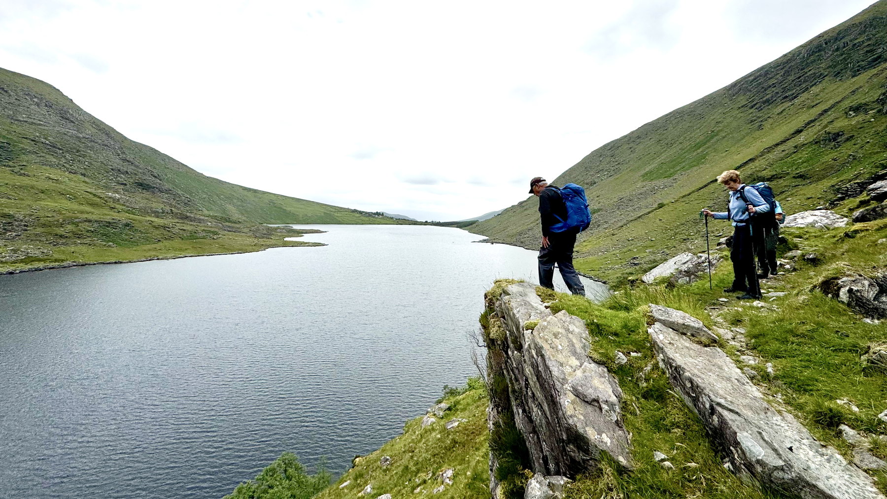 Walkers standing on rock above the still edge of Coomacullen lake
