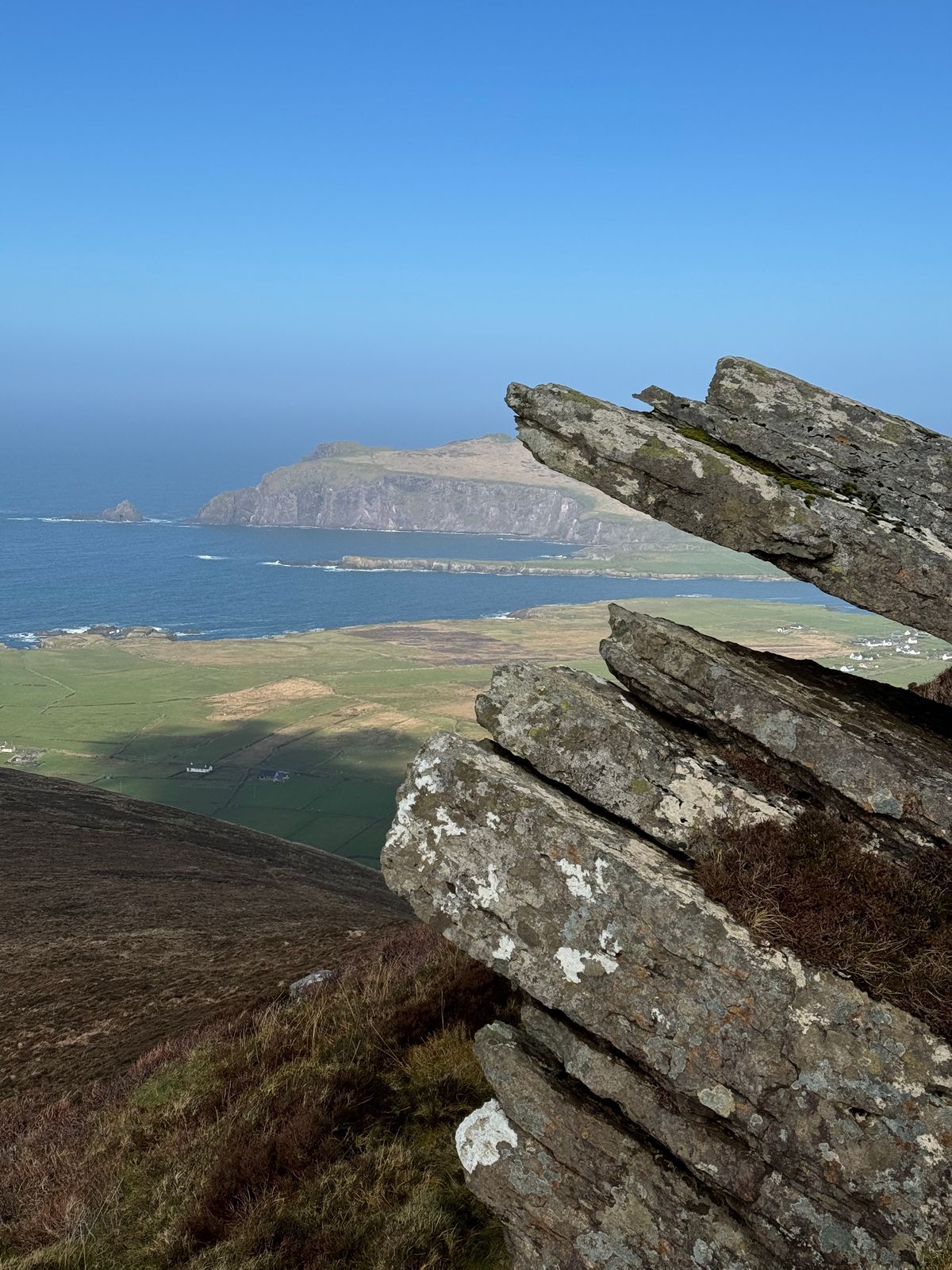 Layered summit rocks with a green headland and sea in the background