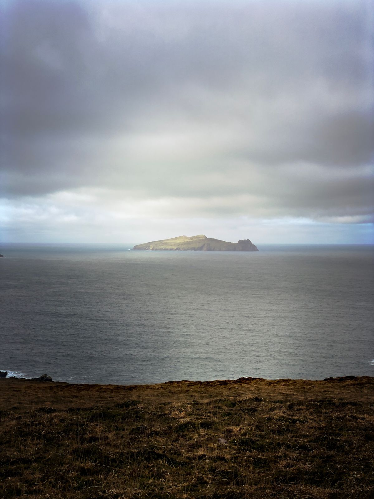 An island across dark water beneath heavy cloud and a shaft of light