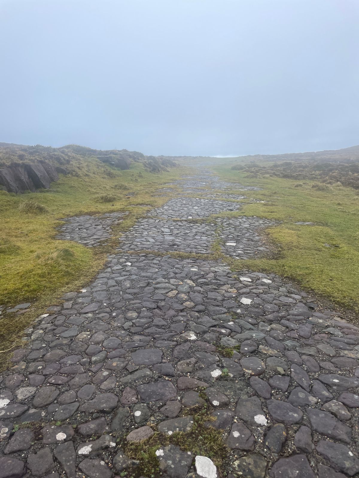 The cobbled street of the Kirrary film set disappearing into mist between grassy banks