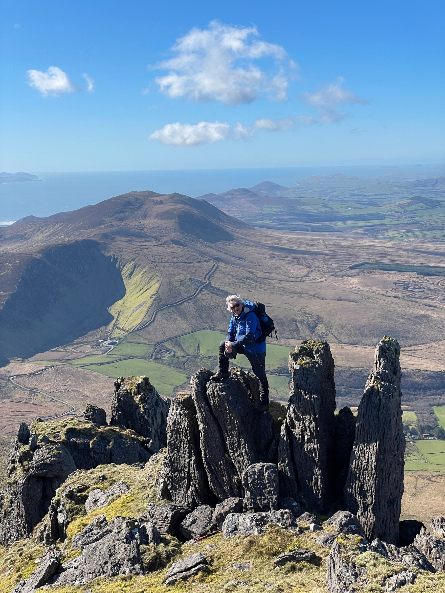 A walker crossing jagged rock with the Derrymore landscape far below