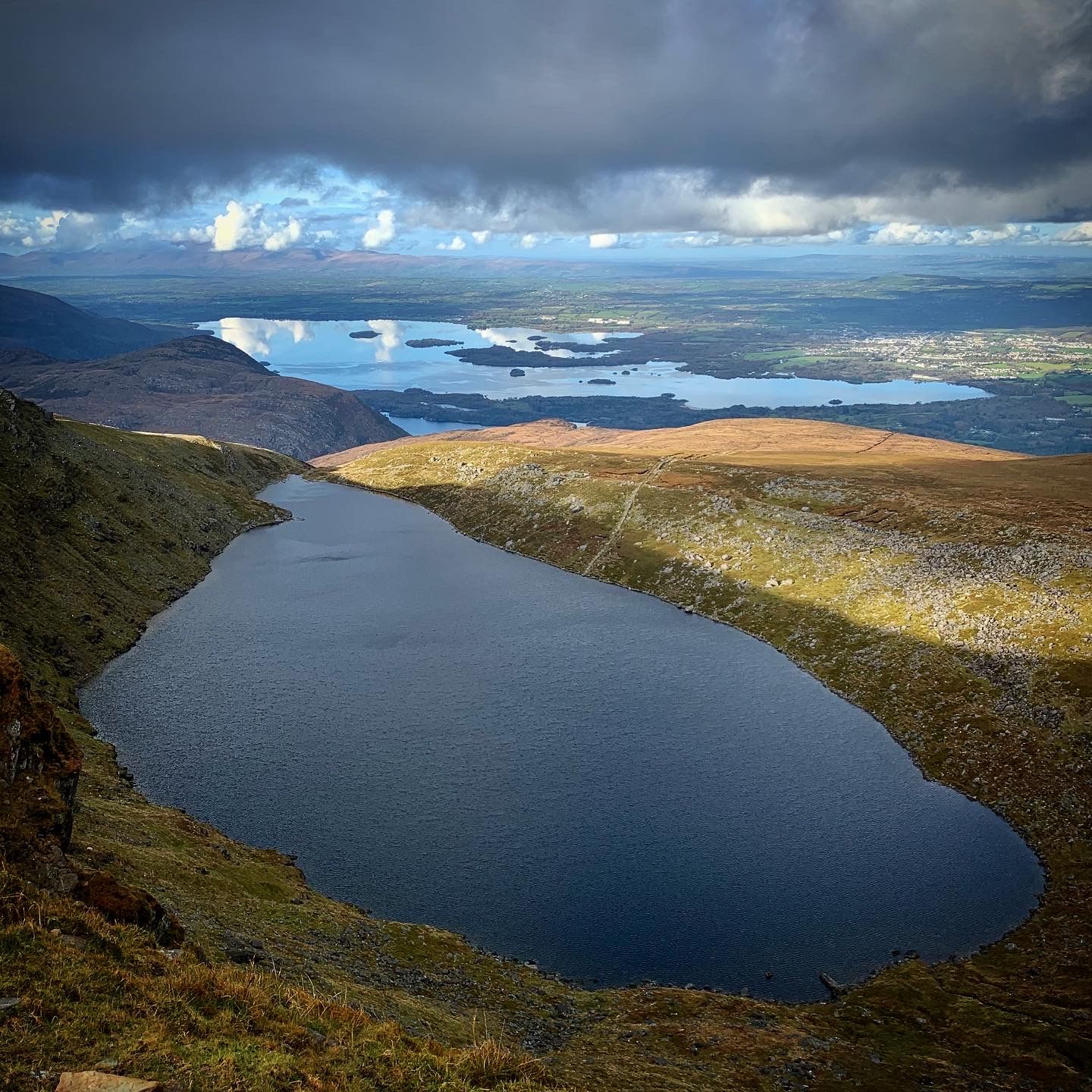 A long mountain lake below dark slopes with the Killarney lakes and islands beyond