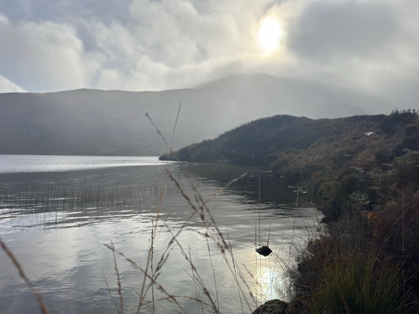 Sunlight breaking through cloud and reflecting on still water beneath the hillside