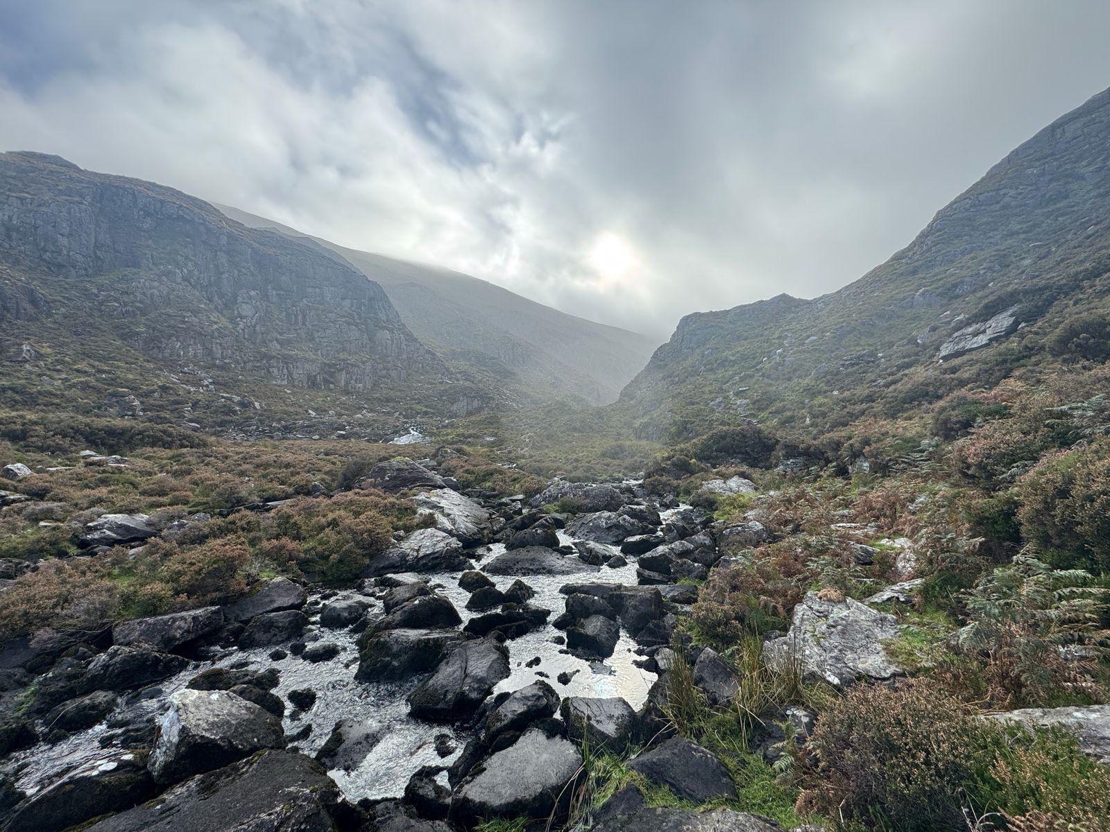 A rocky stream running down a steep-sided glen beneath low cloud