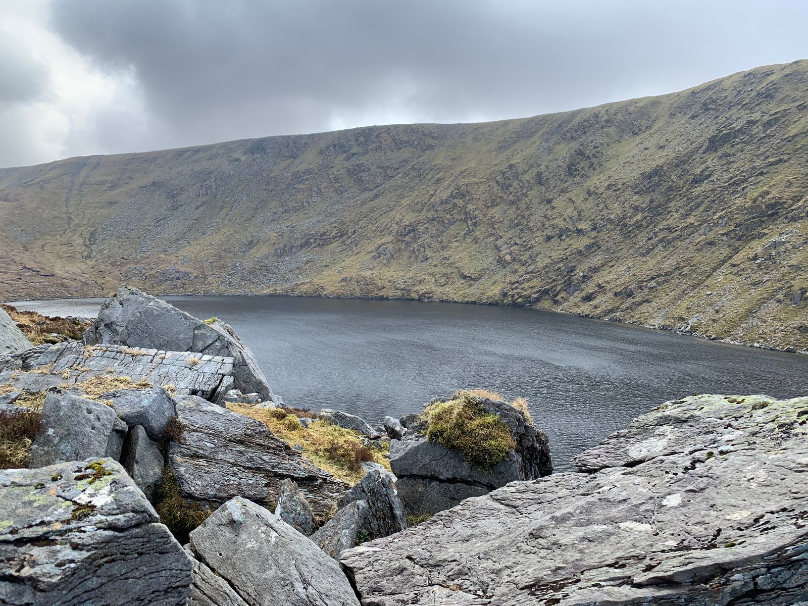Large grey boulders beside a dark lake enclosed by steep mountain slopes
