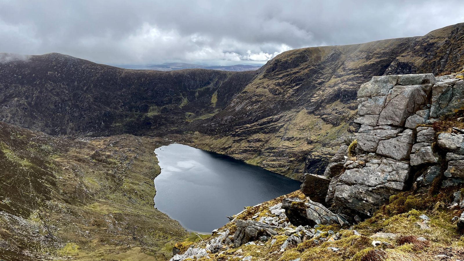 A mountain lake enclosed by high corrie walls with fractured rock in the foreground
