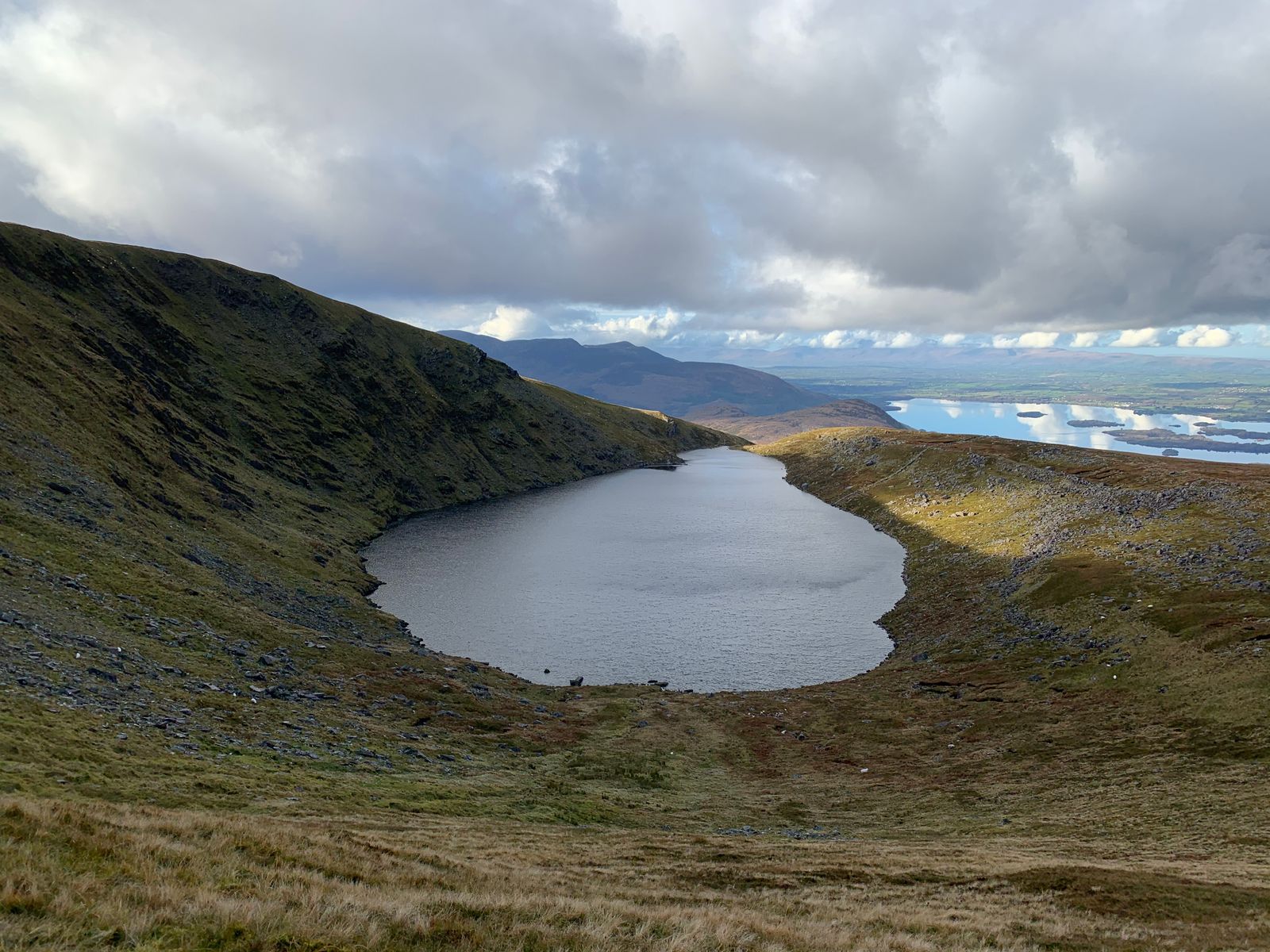 A long dark lake between mountain slopes with sunlit islands in the distance
