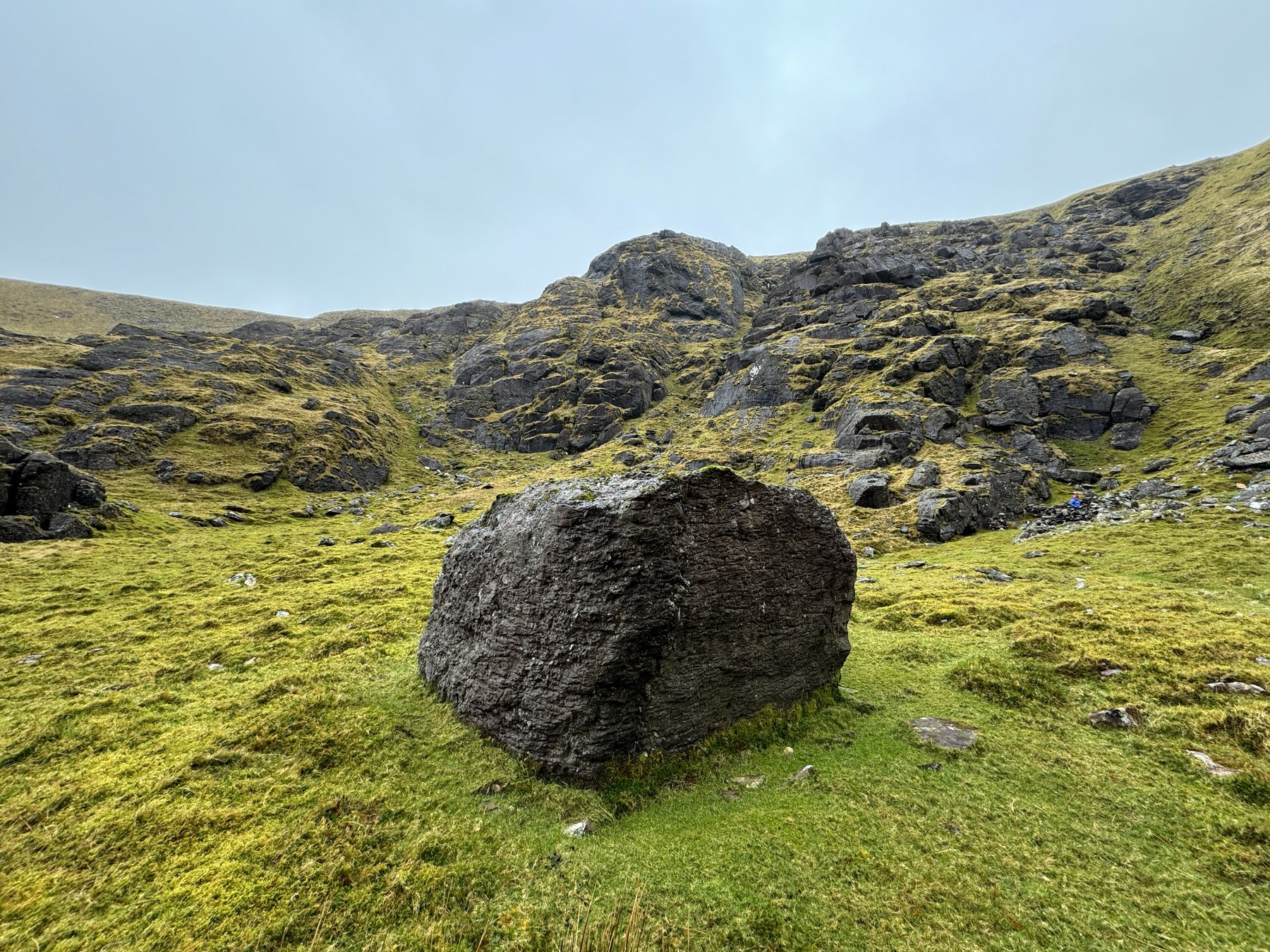 A large rectangular rock standing below the broken cliffs of Derrymore Glen