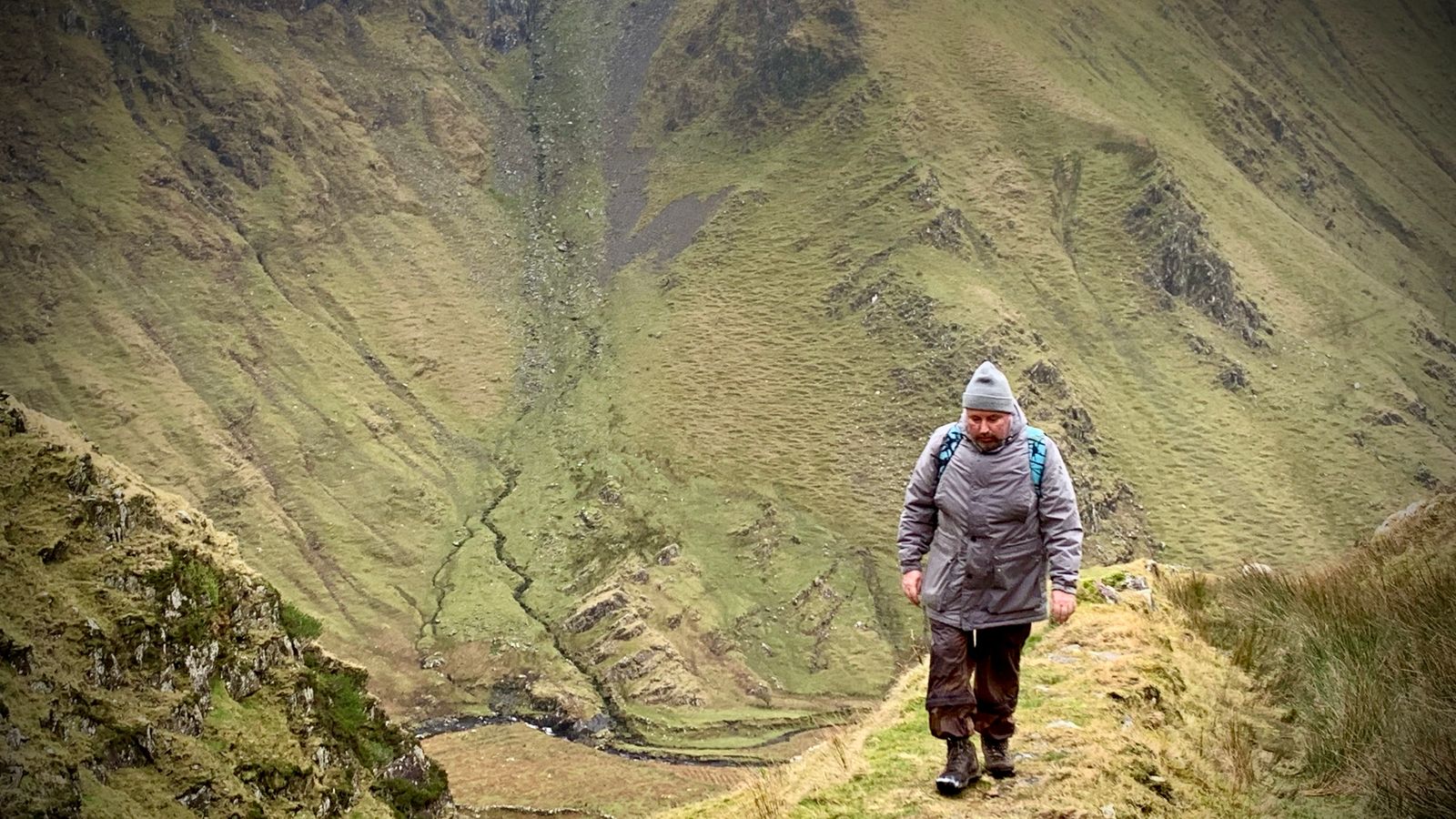 A walker crossing steep grassy ground high above the river in Macha na Bó