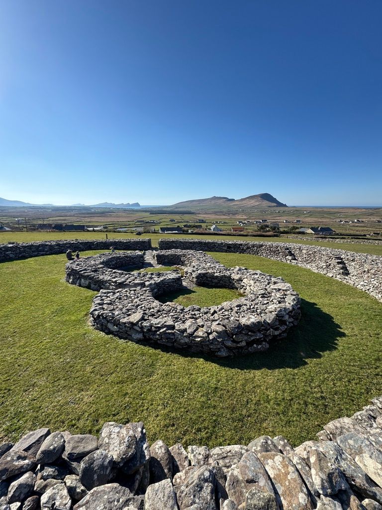 Drystone cashel wall enclosing a pair of conjoined hut foundations, with the western headlands beyond