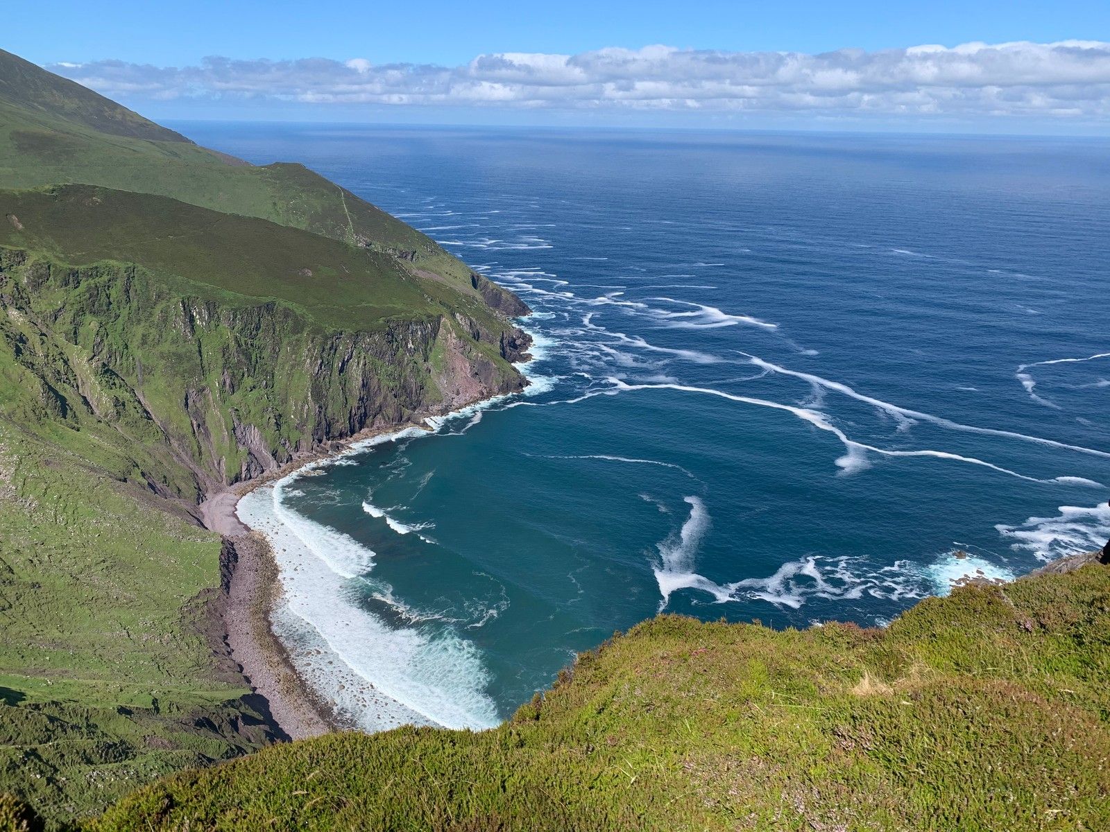 A broad view across the green cliffs, cove and breaking Atlantic swell