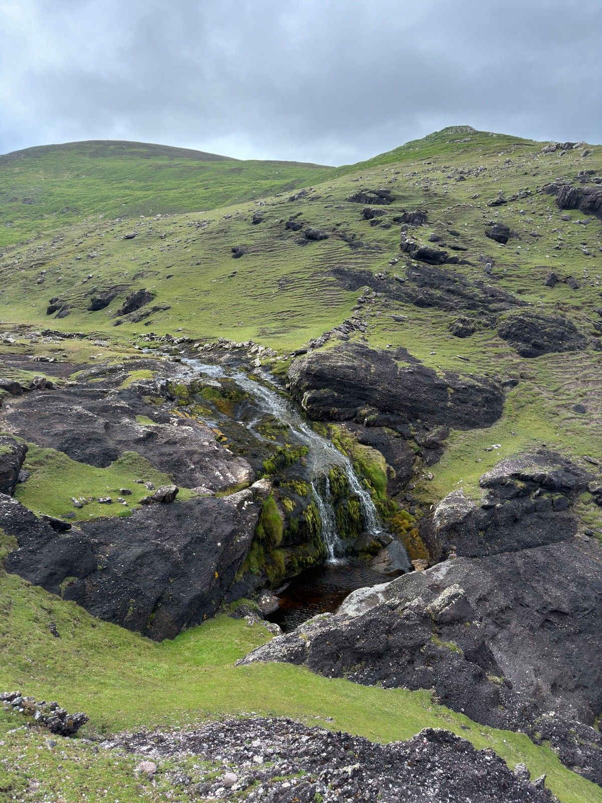A coastal cascade running through green rocky hillside towards the Atlantic cliffs
