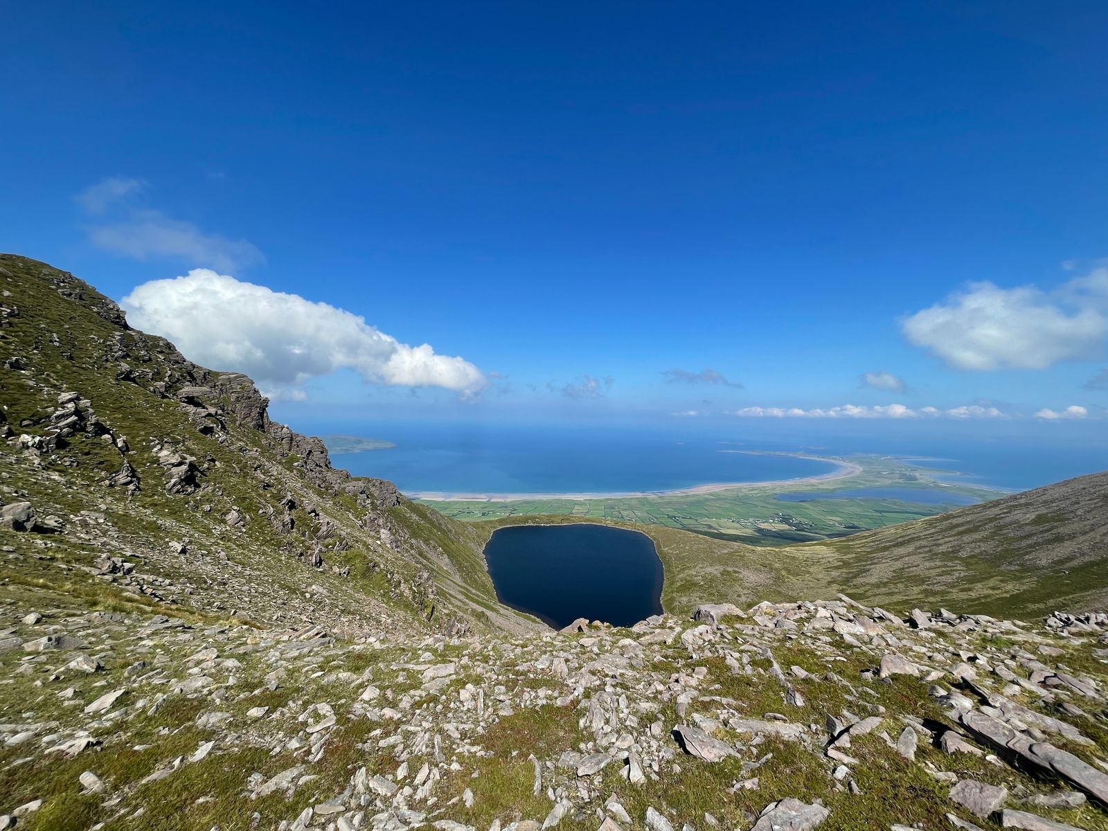 A view down a rocky hollow towards Lough Acummeen and blue Brandon Bay