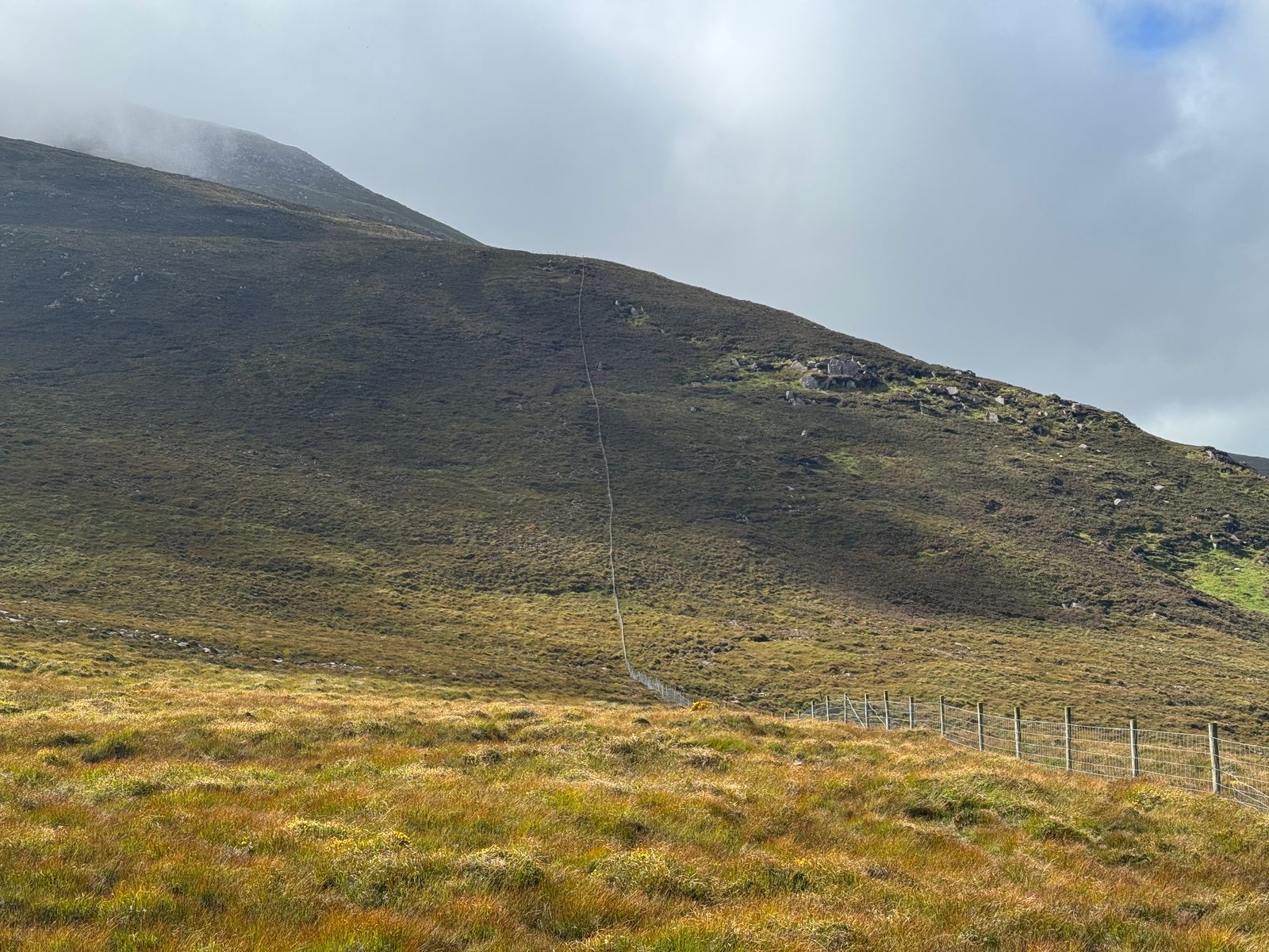 Mist over the upper mountain above grassy slopes, rocks and a fence