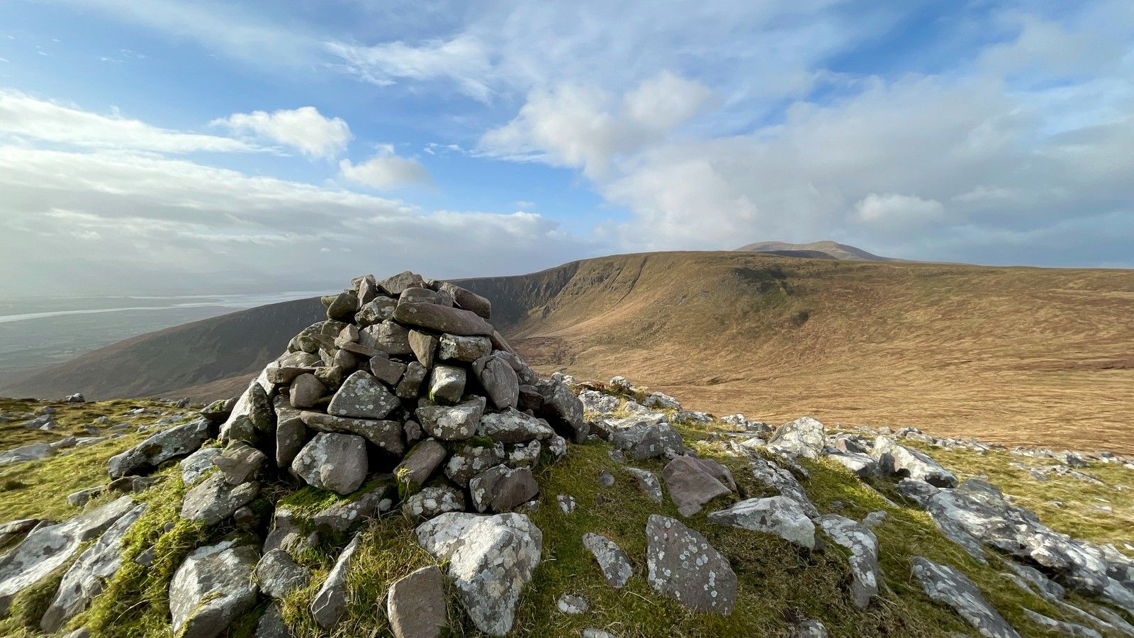 A broad mountain panorama centred on a stone cairn with Tralee Bay in the distance