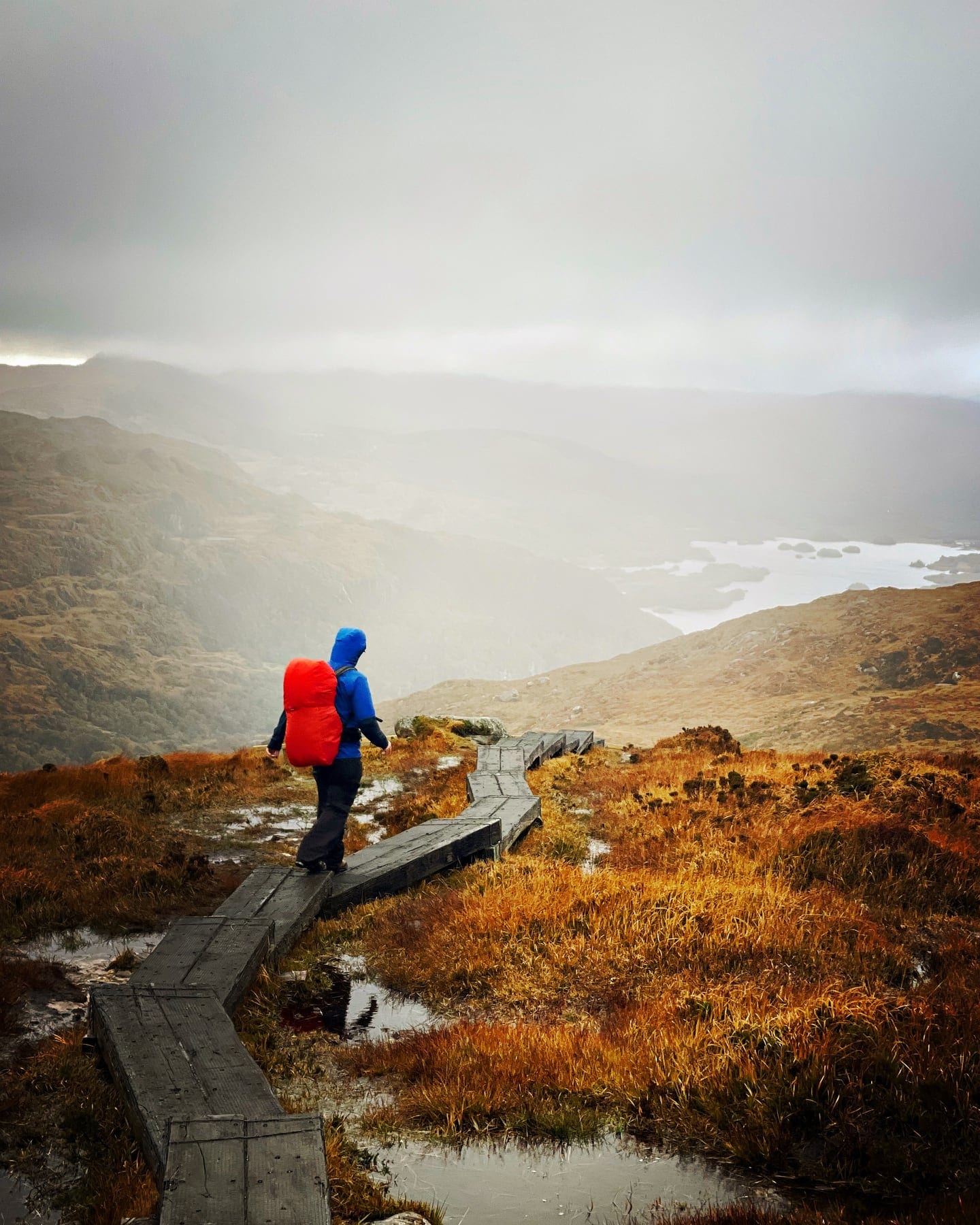 A hiker descending a mountain boardwalk in dramatic light above the lakes